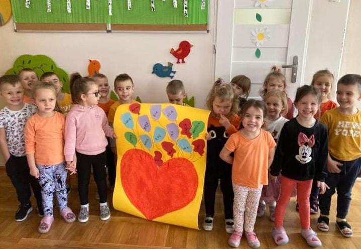 Dzieci stoją w grupie trzymając plakat z namalowanym pomarańczowym sercem.