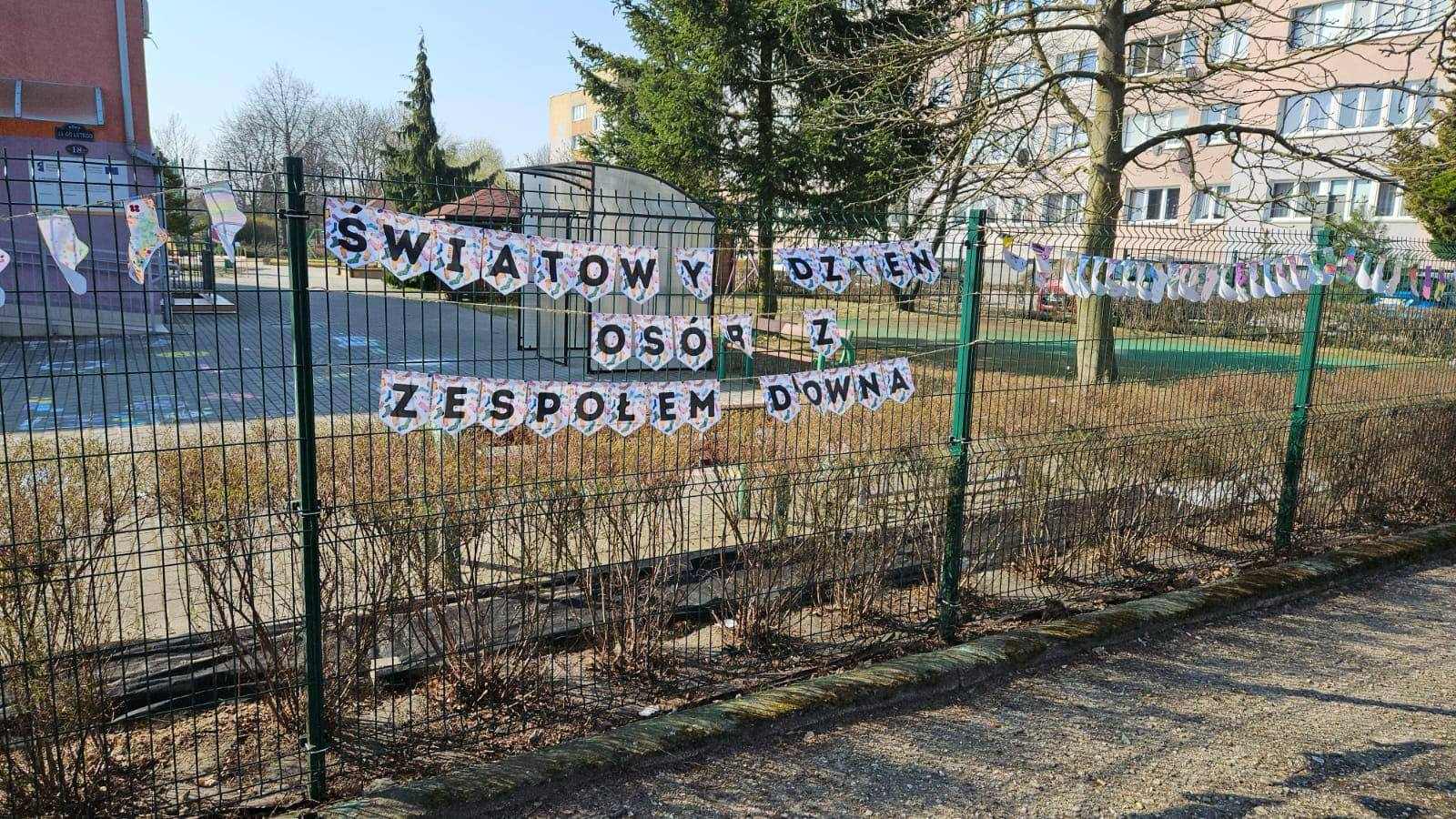 Skarpetki wykonane z papieru wiszą na sznurku na płocie przedszkola oraz napis światowy dzień os&oacute;b z zespołem downa..