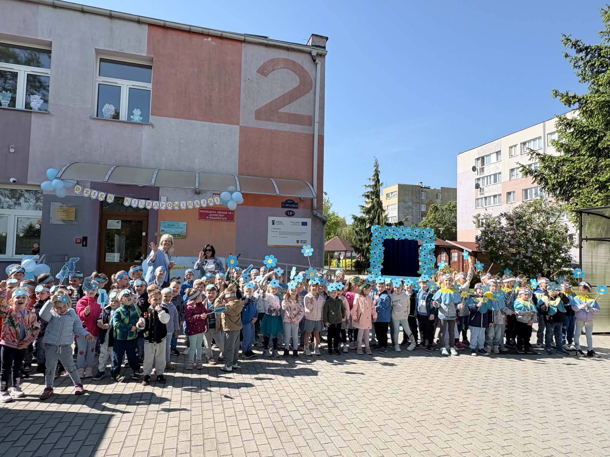 Wszystkie dzieci ubrane na niebiesko stoją w grupie przed przedszkolem.