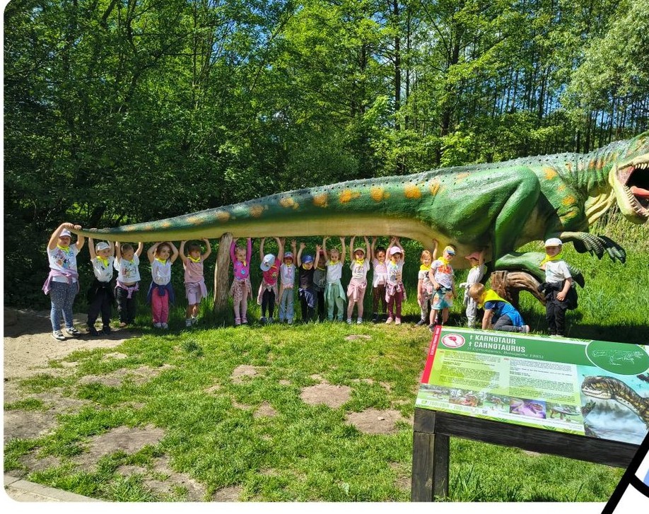 Dzieci stoją w rzędzie pod dinozaurem.