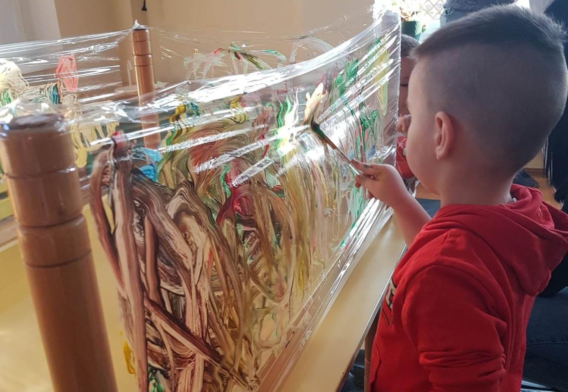 Chłopiec maluje farbami na folii.