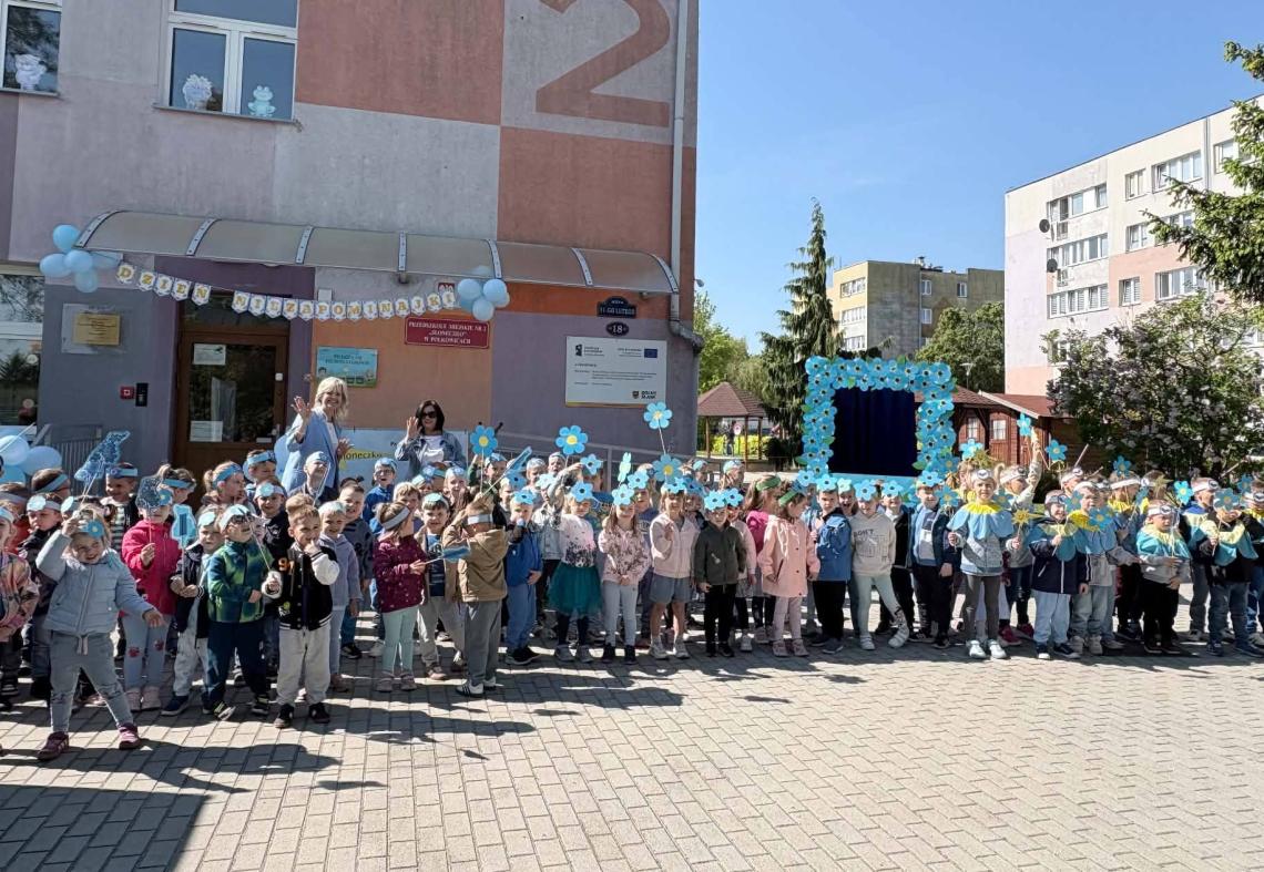 Wszystkie dzieci ubrane na niebiesko stoją w grupie przed przedszkolem.