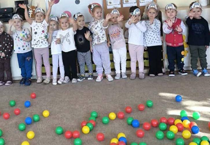 Dzieci stoją w grupie przed nimi kolorowe kulki.