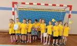 Grupa dzieci ubrana na sportowo w żółte bluzki stoi w bramce trzymając dyplom i puchar.