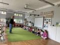 Dzieci siedzą w półkolu na dywanie razem z aktorką.