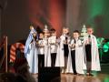 Pięcioro dzieci w białych pelerynkach stojąc na scenie śpiewają pastorłaki.