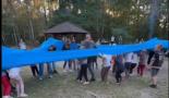 Dzieci w grupie otoczone są niebiską gumą i próbują ją rozciągnąć.